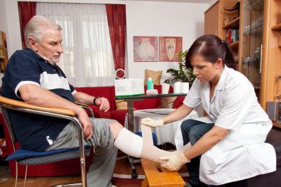 caregiver putting medical bandage on the foot of the senior man
